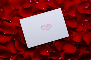 Different red petals of roses and postcard with mark of lips. Flat lay