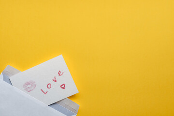 Handmade postcard with mark of lips and lettering love from envelope on yellow background