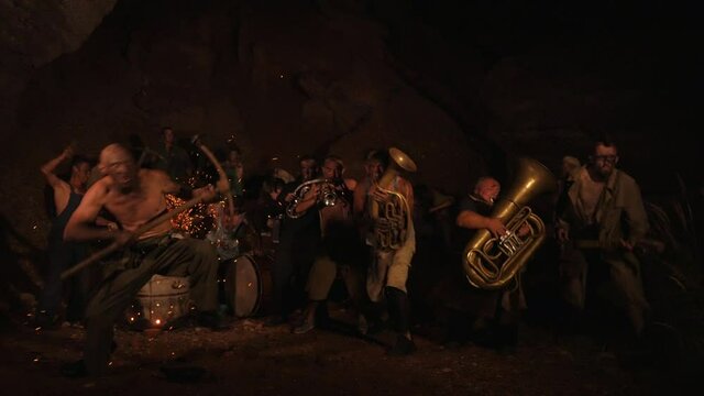Funny musicians play underground in a cave at night. Crazy people play musical instruments and dance funny dances in the cave. Funny bass guitarist, tubist, trumpeter, drummer.