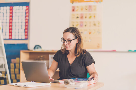 Female teacher typing on her laptop in her classroom.