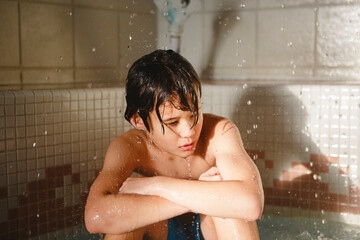 A beautiful boy sits in a pool with water drops falling around him
