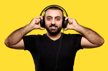 Positive bearded DJ with headphones laughing on a yellow background. Enjoy your music. International DJ Day.