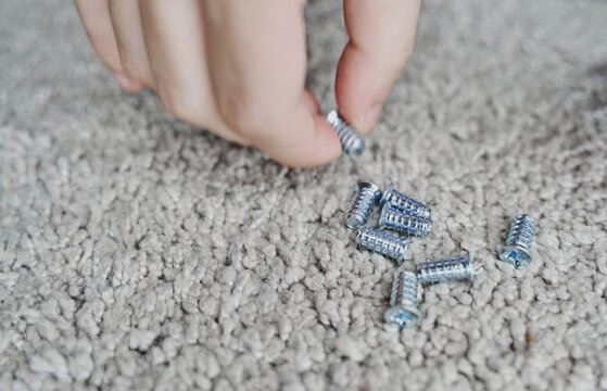 Close up of a caucasian hand picking a metallic screw of a group of several screws from the floor. Horizontal photo