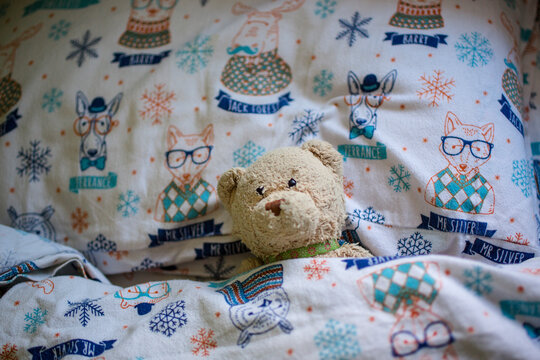 A child's stuffed bear toy lays lovingly tucked into cozy bed