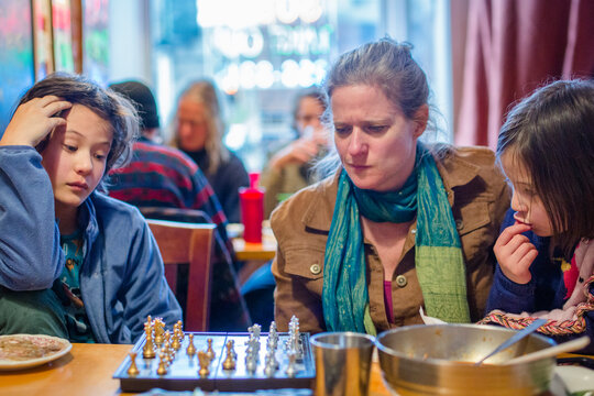 A woman and children sit together in restaurant studying chess board
