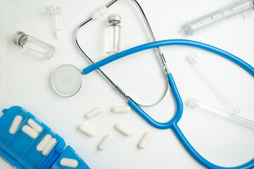 Medical layout on white background, flat lay. Blue stethoscope or phonendoscope surrounded by capsules, ampoules and test tubes.