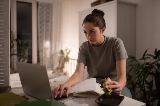 Student with sandwich typing on laptop at home