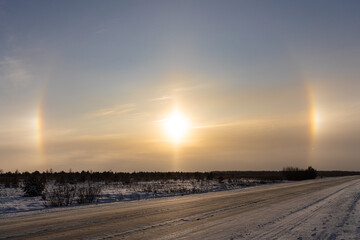 Snowy deserted road in winter on the orange a natural phenomenon halo glow background