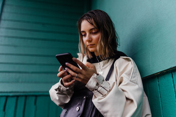 Drenched woman with phones, near a green wall