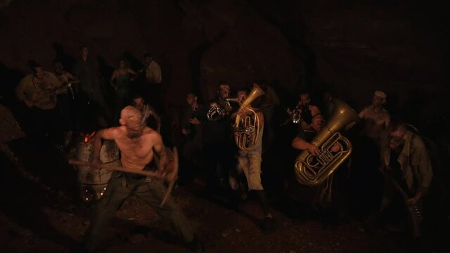 Crazy orchestra playing. Funny musicians play underground in a cave at night. Crazy people play musical instruments and dance funny dances in the cave. Funny bass guitarist, tubist, trumpeter, drummer