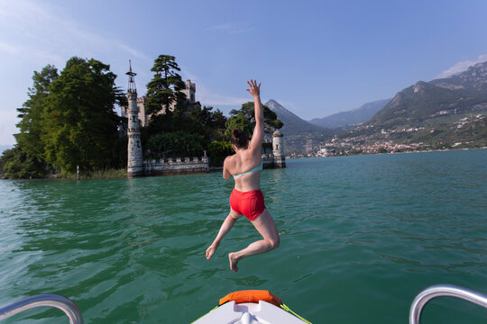 Leaping into a turquoise lake and fortress island in background, Italy