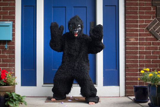 A boy wearing a gorilla suit and mask stands barefoot on front stoop