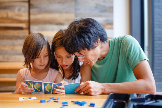 A father plays a board game with his daughters at a wooden table