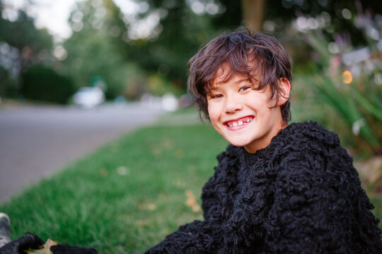 A happy boy in a gorilla suit smiles and sits in a grassy yard