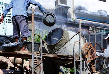 Construction workers pouring cement, sandstone and water into the mortar mixer.