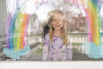 smiling blond young girl under rainbow painted on window