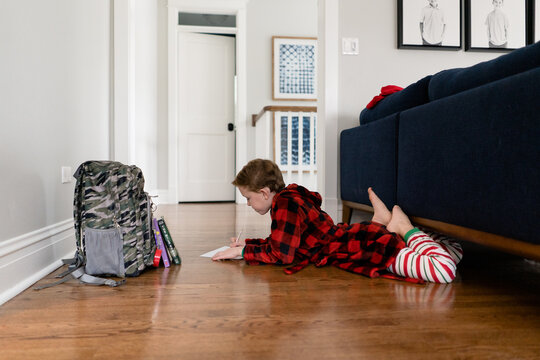 side view of boy coloring laying on floor indoors in pajamas and robe