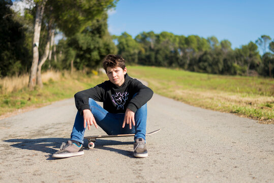 Handsome teen male with a skateboard sitting on asphalt road