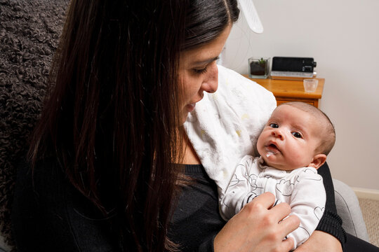 A mother sits in a chair and holds her newborn son and looks at him