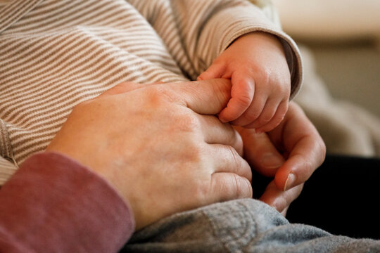 A 2 month old baby boy holds his moms finger with his tiny hand
