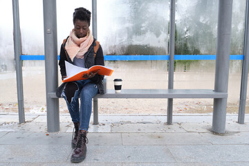 University female african student studying her lecture notes while is waiting for a bus on campus. College life concept.
