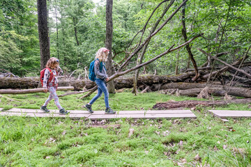 two girls walking across wood planks while hiking together in spring