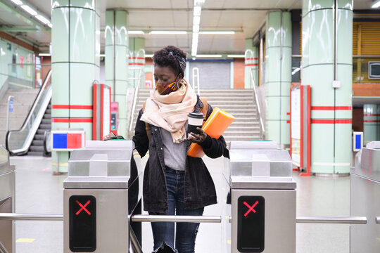 University female african student wearing protective face mask passing through the turnstiles with her transport card at the underground station. New normal in public transport.