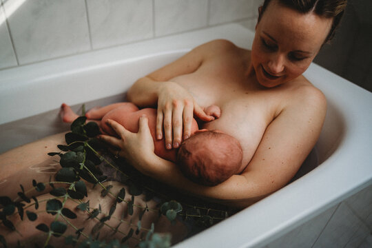 Mother breastfeeding newborn baby in bath tub after birth skin to skin