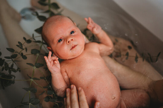 Mother holding newborn baby in bath tub in home birth with eucalyptus