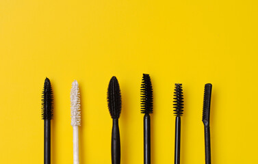 Various types of mascara wands on yellow surface