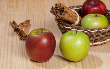 Red and green apple with a cinnamon stick; photo on wooden background.