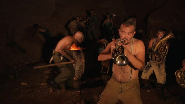 Crazy orchestra playing. Funny musicians play underground in a cave at night. Crazy people play musical instruments and dance funny dances in the cave. Funny bass guitarist, tubist, trumpeter, drummer