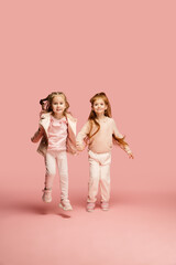 Flying. Happy kids, girls isolated on coral pink studio background. Look happy, cheerful. Copyspace for ad. Childhood, education, emotions, facial expression concept. Jumping, running, having fun