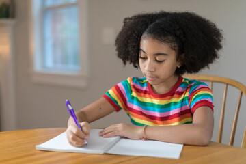 Ten year-old bi-racial girl writing in notebook at table