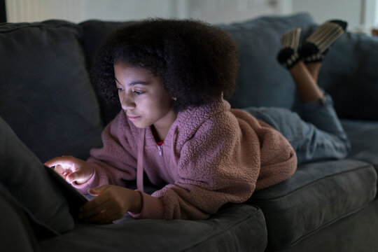 Ten year-old bi-racial girl working on her ipad while lying on sofa