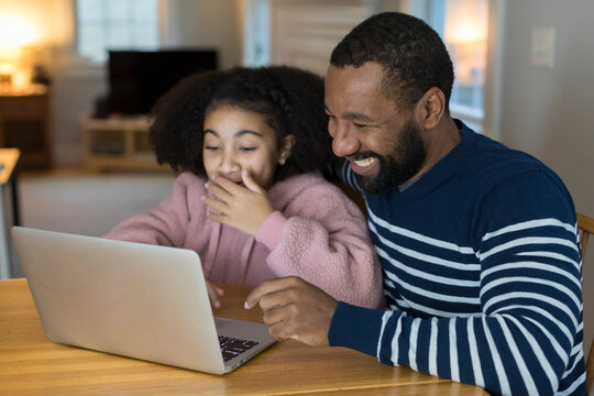 African-American father and tween daughter laugh looking at laptop