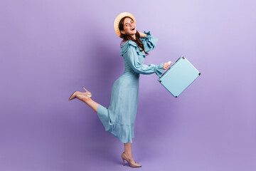 Stylish girl traveler runs on lilac background. Model in hat and heels keeps satchel