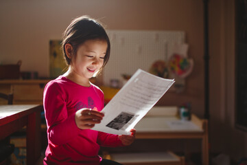 A smiling child in beautiful light studies a piece of paper, reading