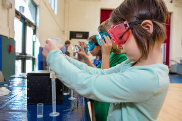 A little girl in safety goggles measures liquid into a test tube