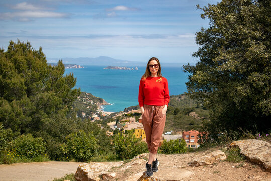 Cheerful girl dressed in red enjoying the coast and looking at the sea