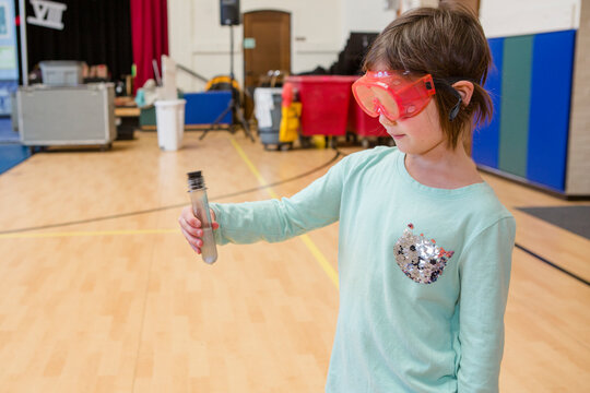 A cute little girl with safety goggles carefully observes a test tube