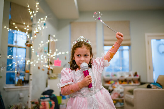 Young girl playing dress up singing in microphone with christmas tree