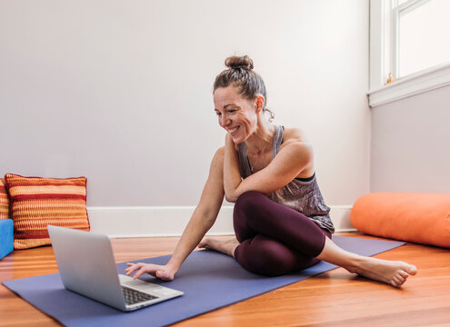 Smiling woman in yoga clothing uses laptop to workout in her home