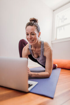 Woman smiles while using computer to practice yoga in her home