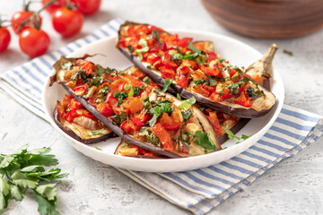 Baked eggplant with tomatoes, peppers, onions, parsley, and olive oil in a plate on a gray concrete table close-up. Tasty vegetarian food Mediterranean style.
