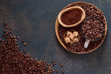 Coffee roasted beans in cup and scattered nearby, ground coffee and cane sugar on a brown table background. Top view with space to copy text.