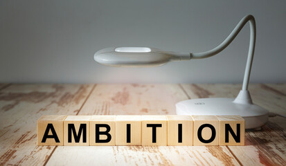 A table lamp illuminates wooden blocks with the word AMBITION