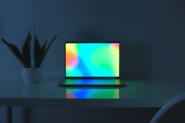 Laptop computer with vibrant sceen standing on a table, low key