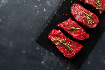 Raw beef steak with spices, onions and rosemary on dark slate or concrete background. Top view