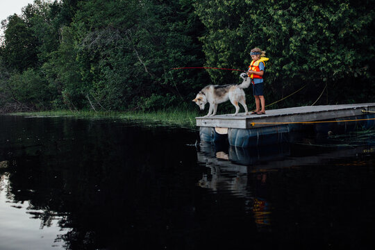 young child fishes on dock with dog